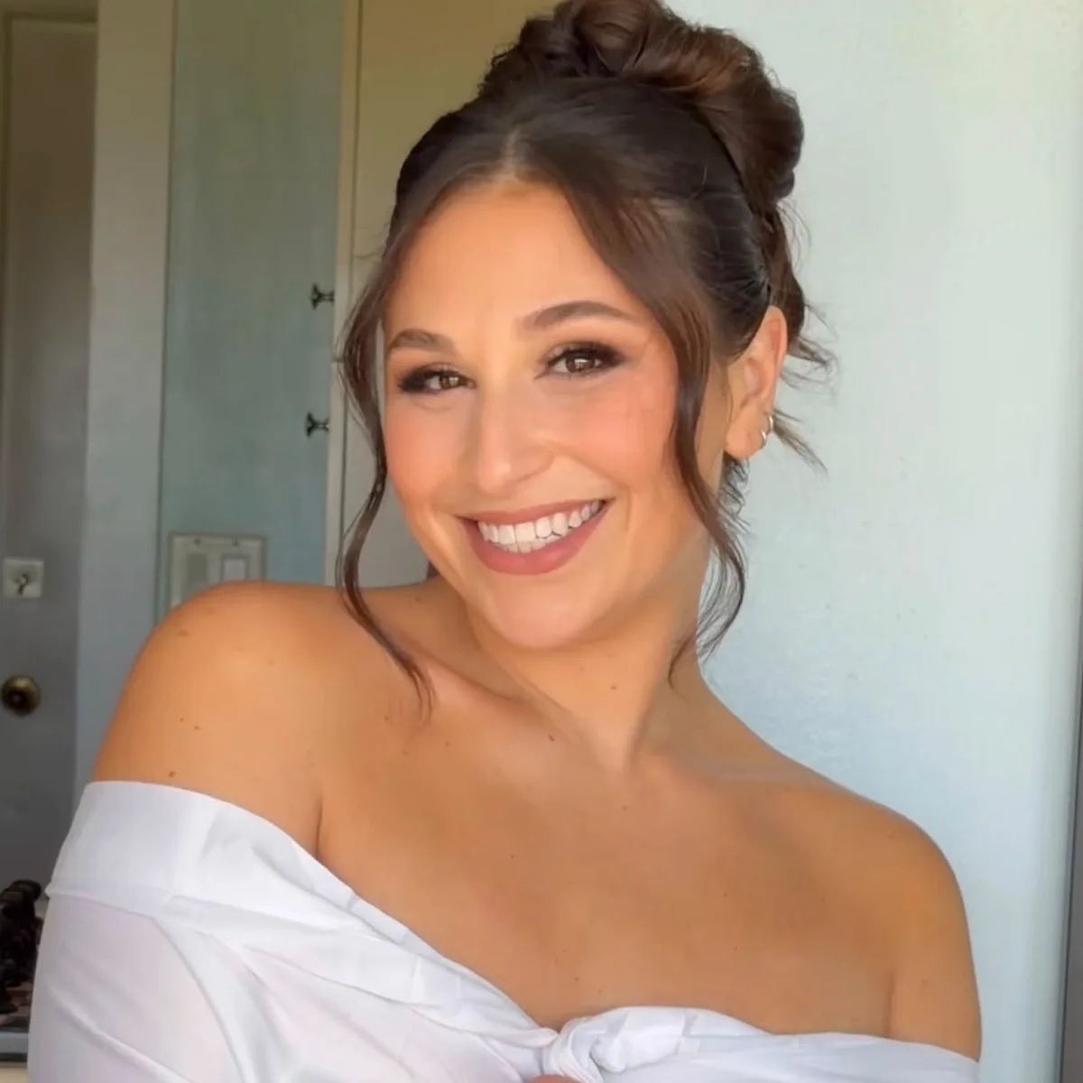 A bride smiling, soft brown glam and a textured updo